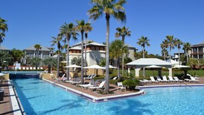 En swimmingpool med solstolar och palmer, omgiven av byggnader.