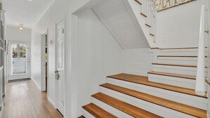 Uma escadaria com degraus de madeira e paredes brancas, conduzindo a um patamar com uma placa que diz "REACH HOUSE".