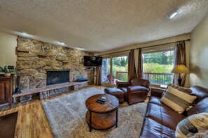 Una sala de estar con chimenea de piedra, sofá de cuero y televisor.