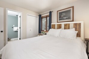 A bedroom with a large bed, a wooden headboard, a framed picture on the wall, and a window with curtains.