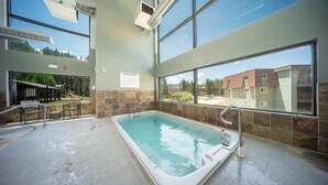 Een wellnessruimte met een jacuzzi, grote ramen en uitzicht op gebouwen.