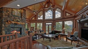 Un salón espacioso con chimenea de piedra, muebles de cuero y ventanas amplias que ofrecen vistas al exterior.