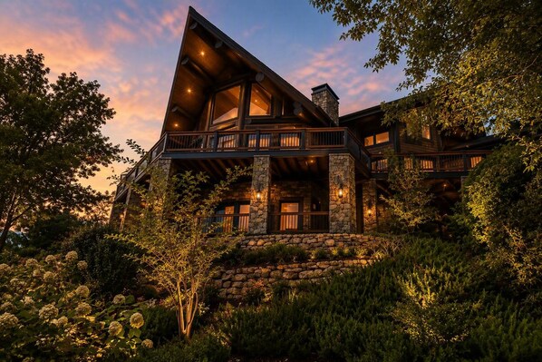 A multi-level cabin with stone exterior walls, multiple balconies, and a stone foundation.