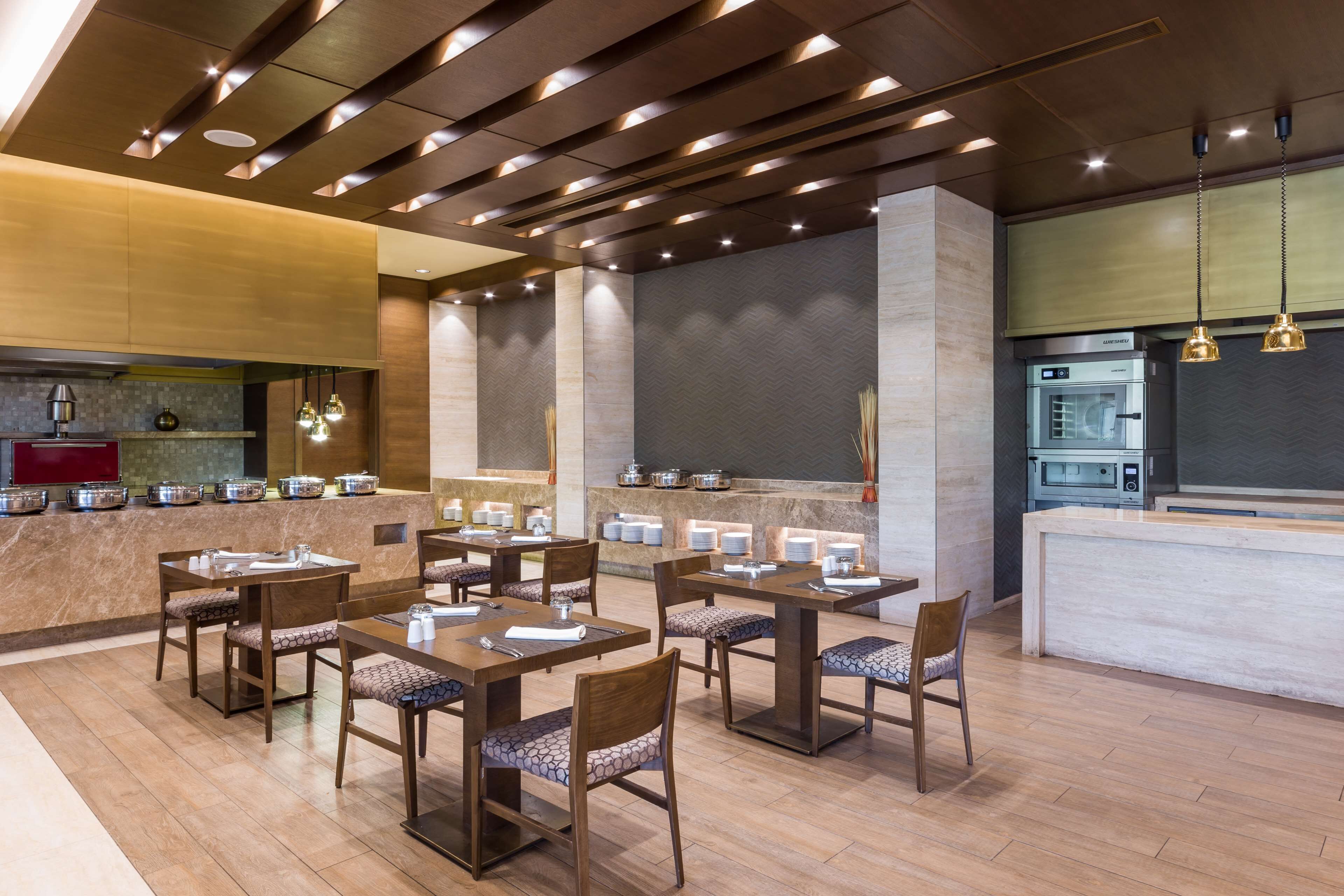 A modern restaurant with multiple dining tables and chairs, a kitchen area, and a bar.