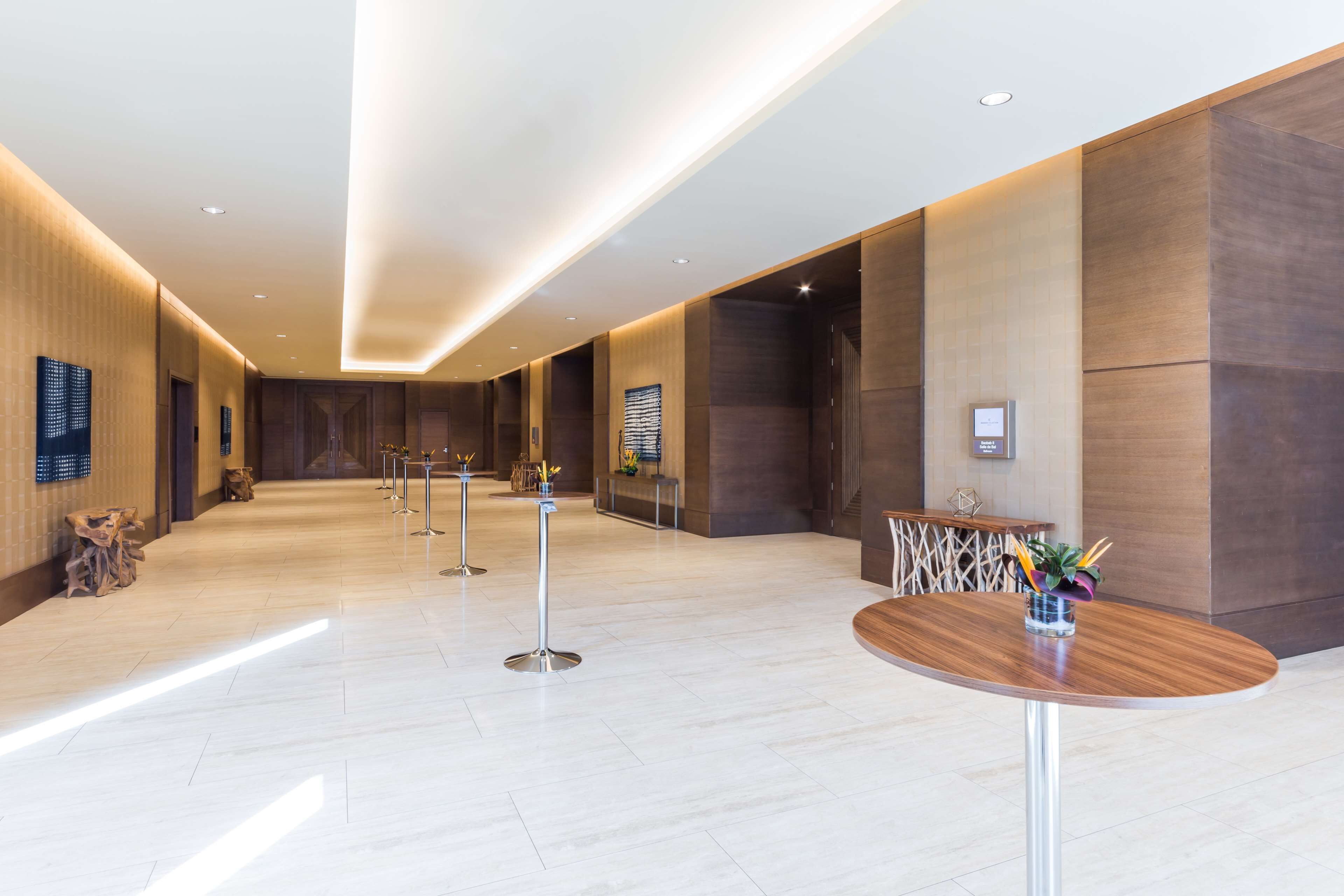 Eine geräumige Lobby mit einer langen Rezeption, einem runden Tisch mit Blumenvase und einem modernen Design aus Holzpaneelen und Einbauleuchten.
