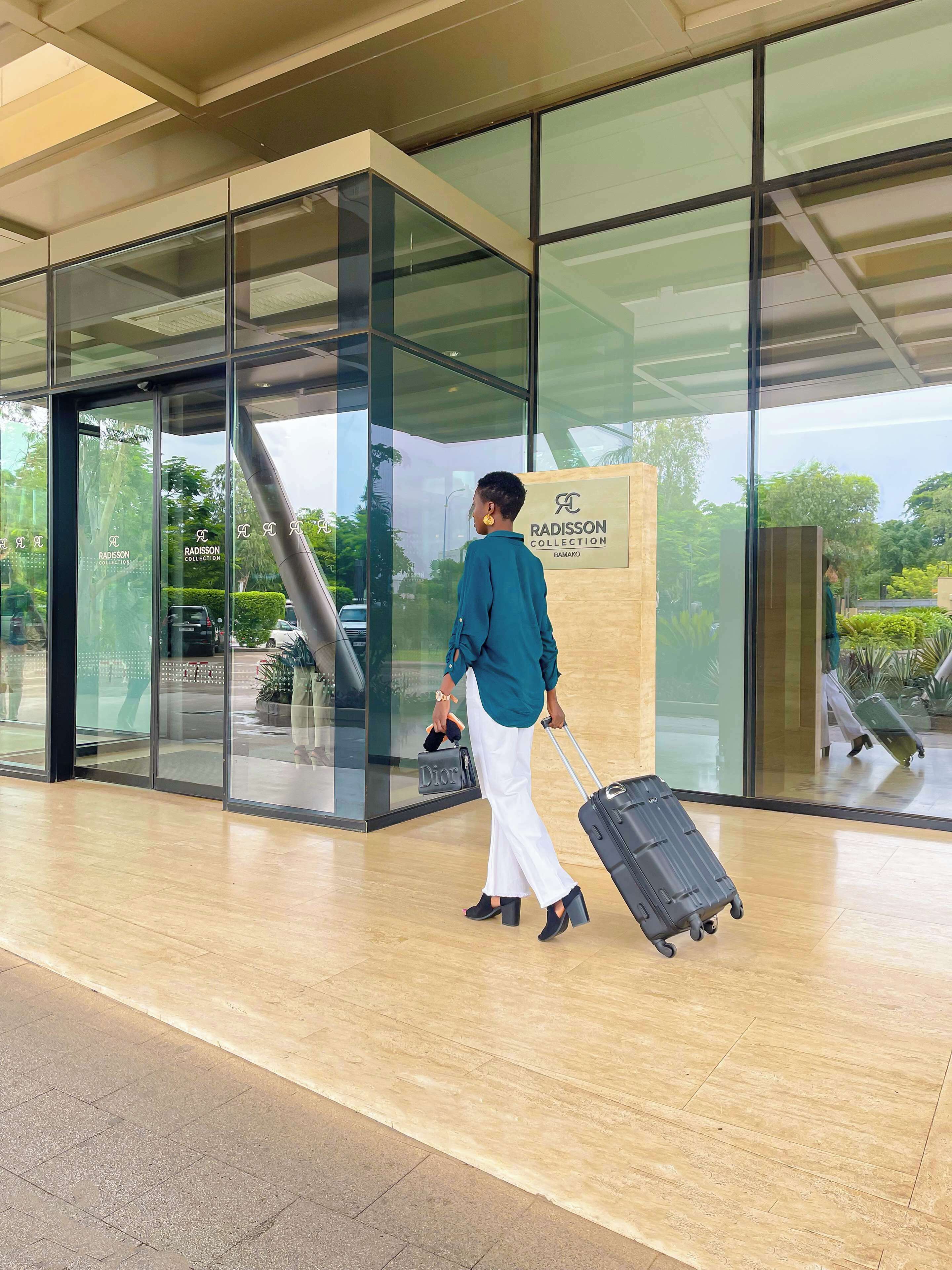 Entrada de un edificio moderno con puertas de cristal, un letrero de Radisson Collection y una persona arrastrando una maleta.