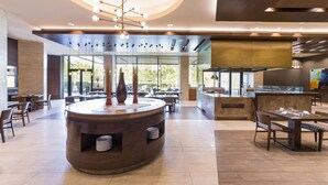A modern restaurant with a central round table, seating arrangements, and a kitchen area.