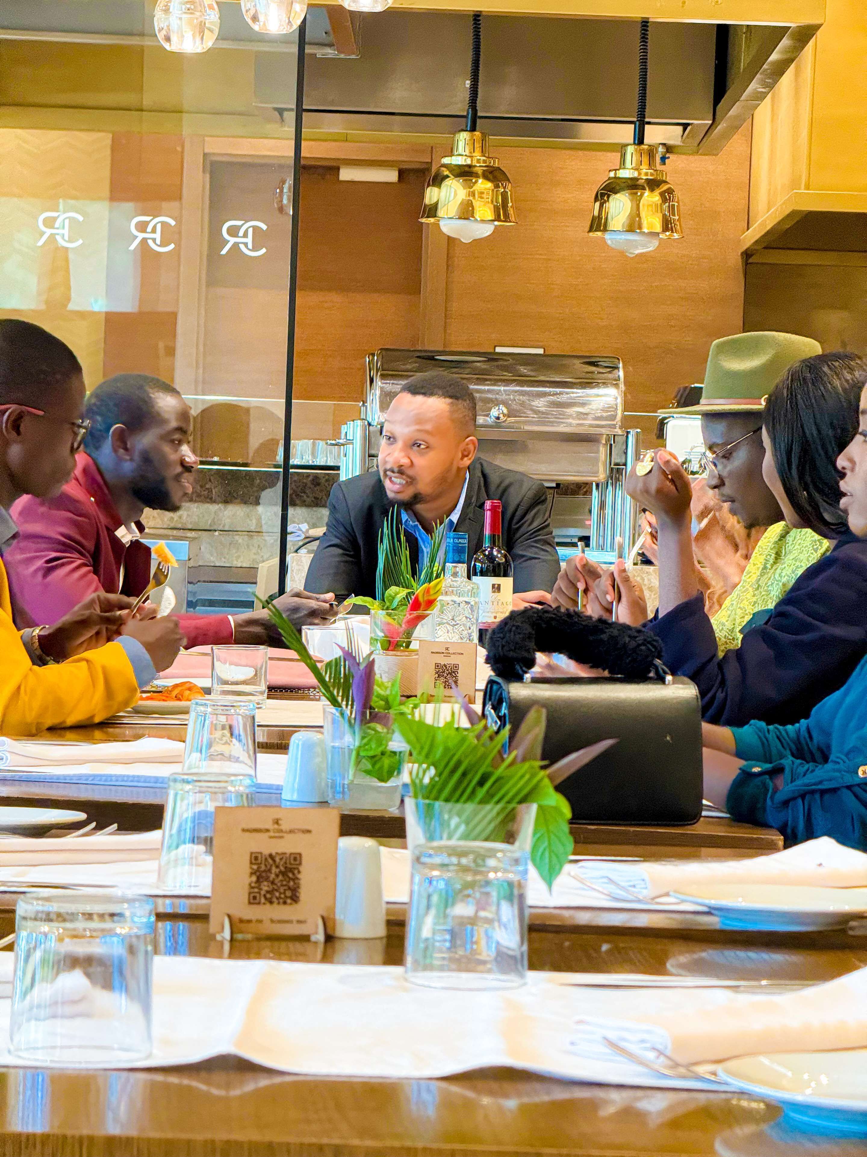 A group of people seated around a table in a restaurant with a modern interior, including pendant lighting and a visible kitchen area.