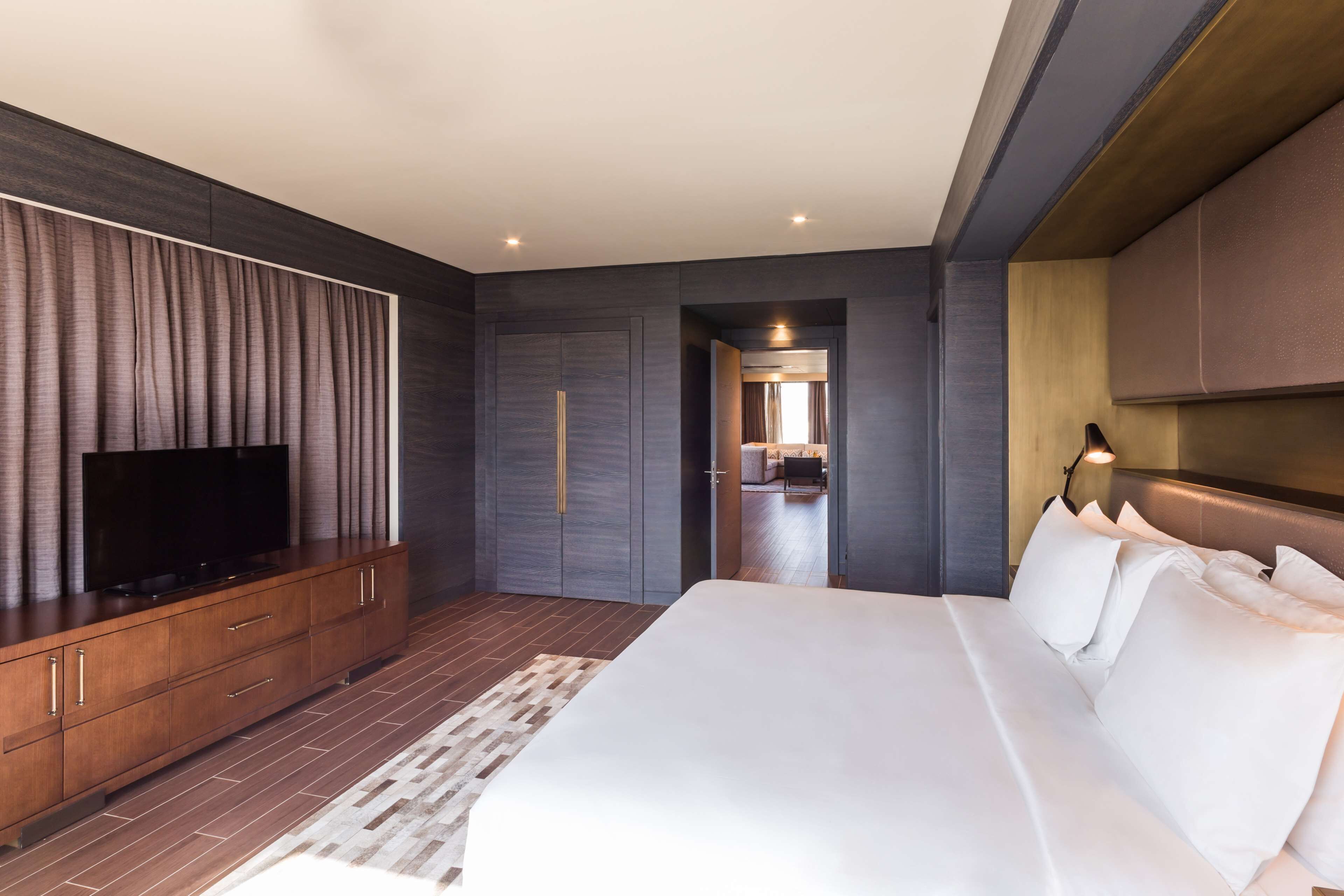 A modern hotel room with a large bed, a flat-screen TV on a wooden console, and a walk-in closet.