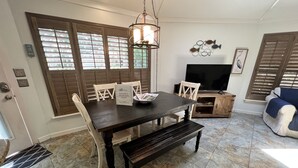 A dining area with a dark wooden table, white chairs, and a bench. There is a television and a decorative fish wall art piece.