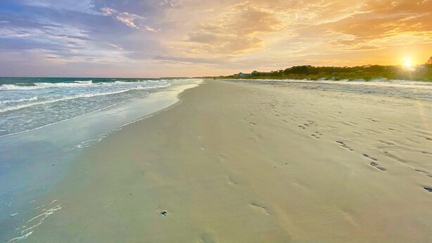 A beach with a long stretch of sand, footprints, and waves.