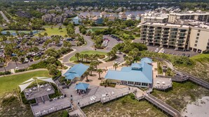 Vista aérea de um resort costeiro com um prédio grande, uma área de praia com um calçadão de madeira e um estacionamento.