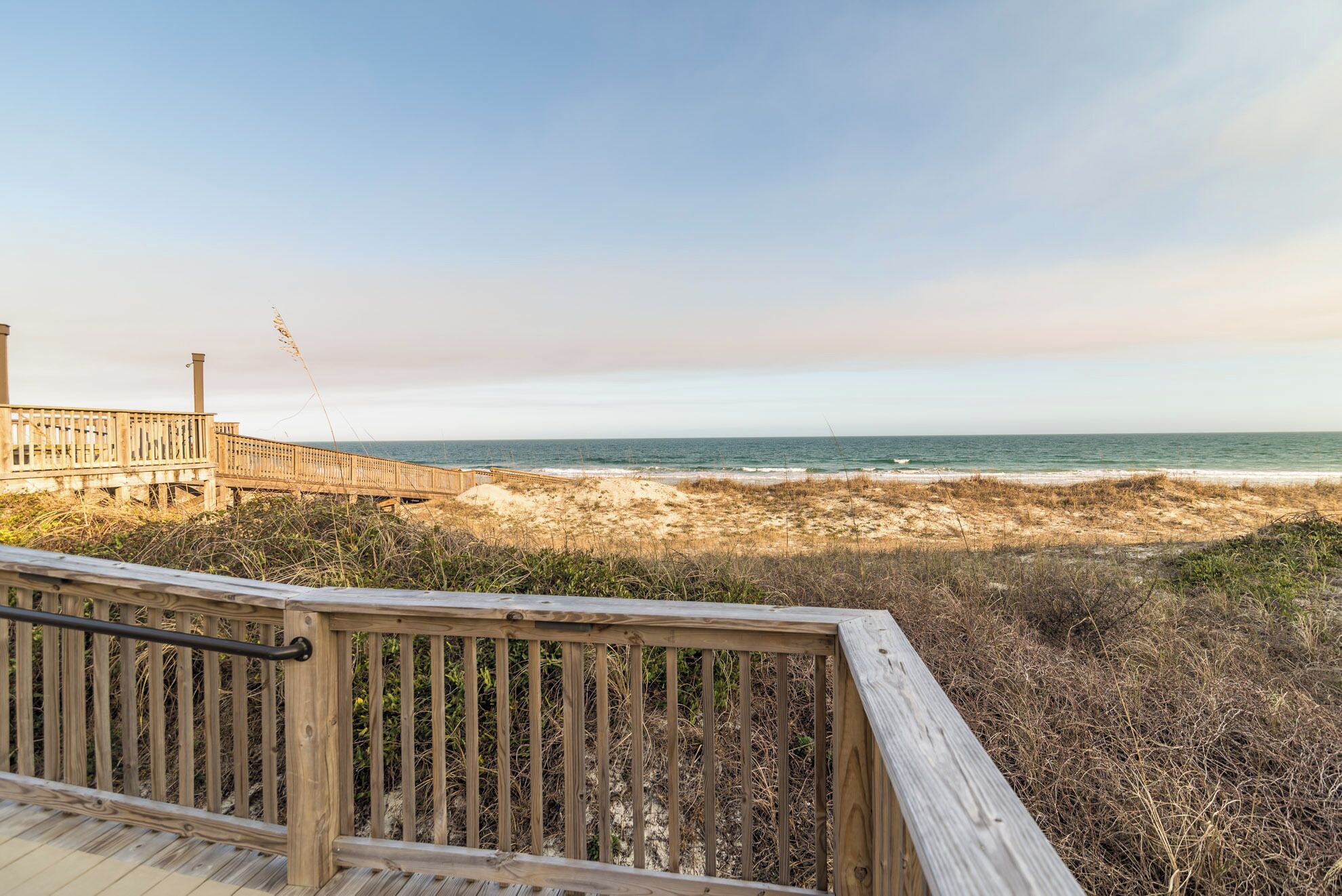 A wooden boardwalk leading to a beach with a clear view of the ocean.