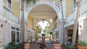 An entrance with a sign reading "The Village of Baytowne Wharf" arching over a brick pathway.
