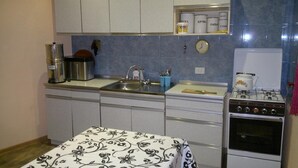 A compact kitchen with a sink, stove, and cabinets. There is a clock on the wall and a shelf with jars. - Guest House Besarioni (Borjomi)