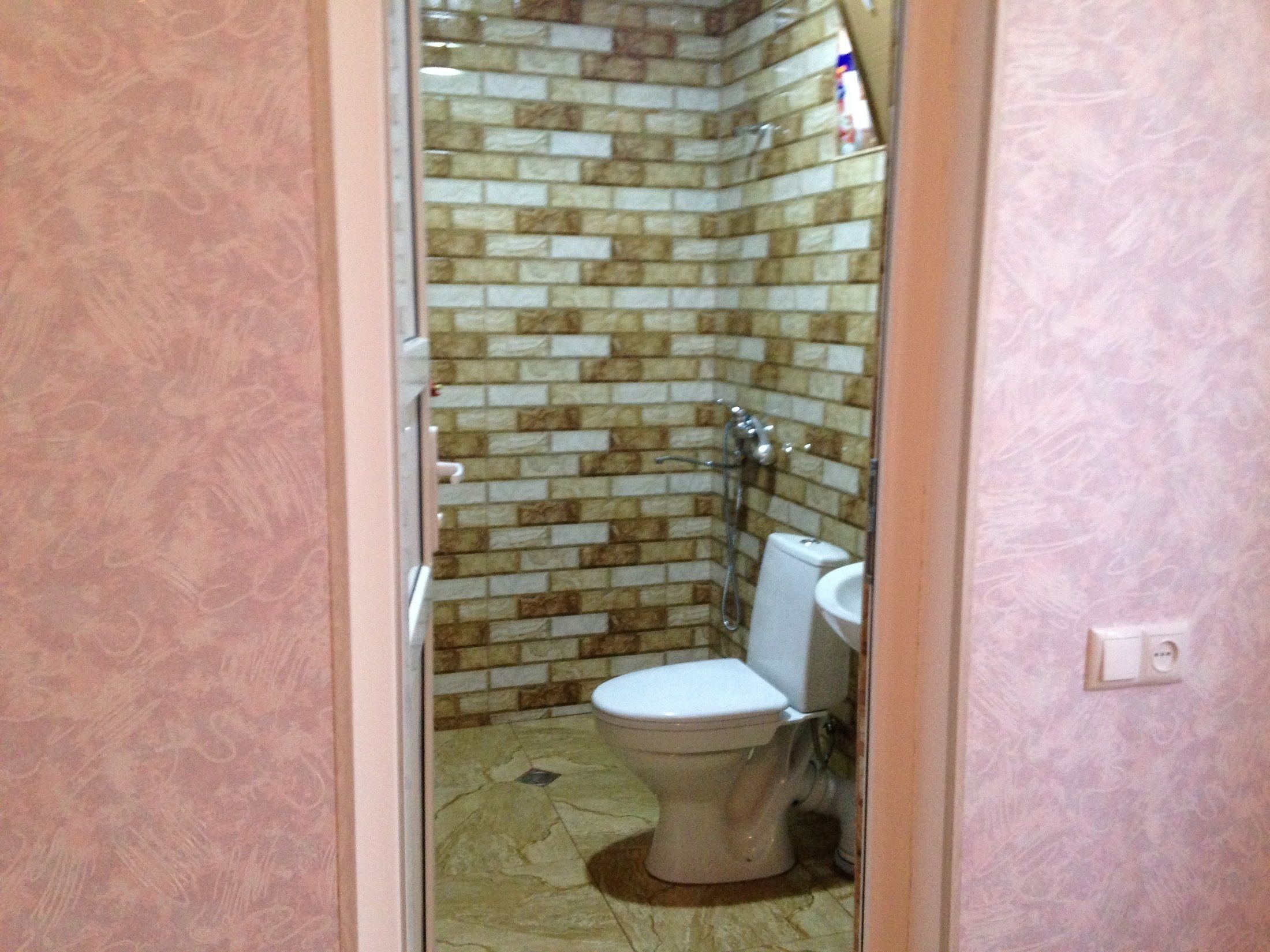 A bathroom with a tiled shower wall, a toilet, and a sink.