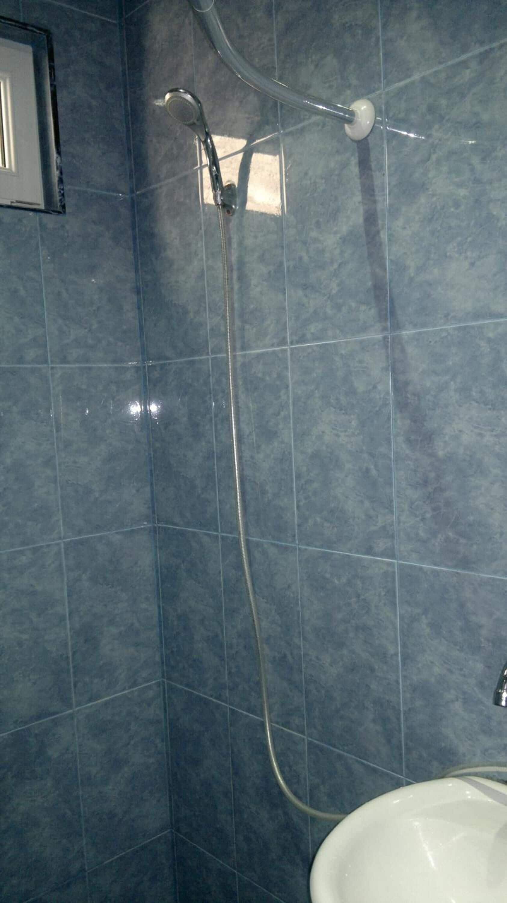 Baño con ducha, paredes de azulejos y lavamanos.