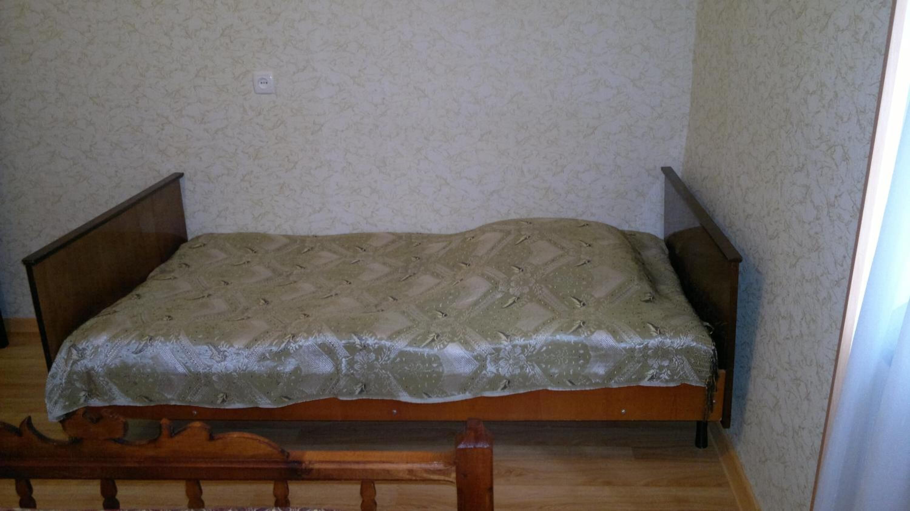 A single bed with a wooden frame and a patterned bedspread in a room with patterned wallpaper and a wooden floor.