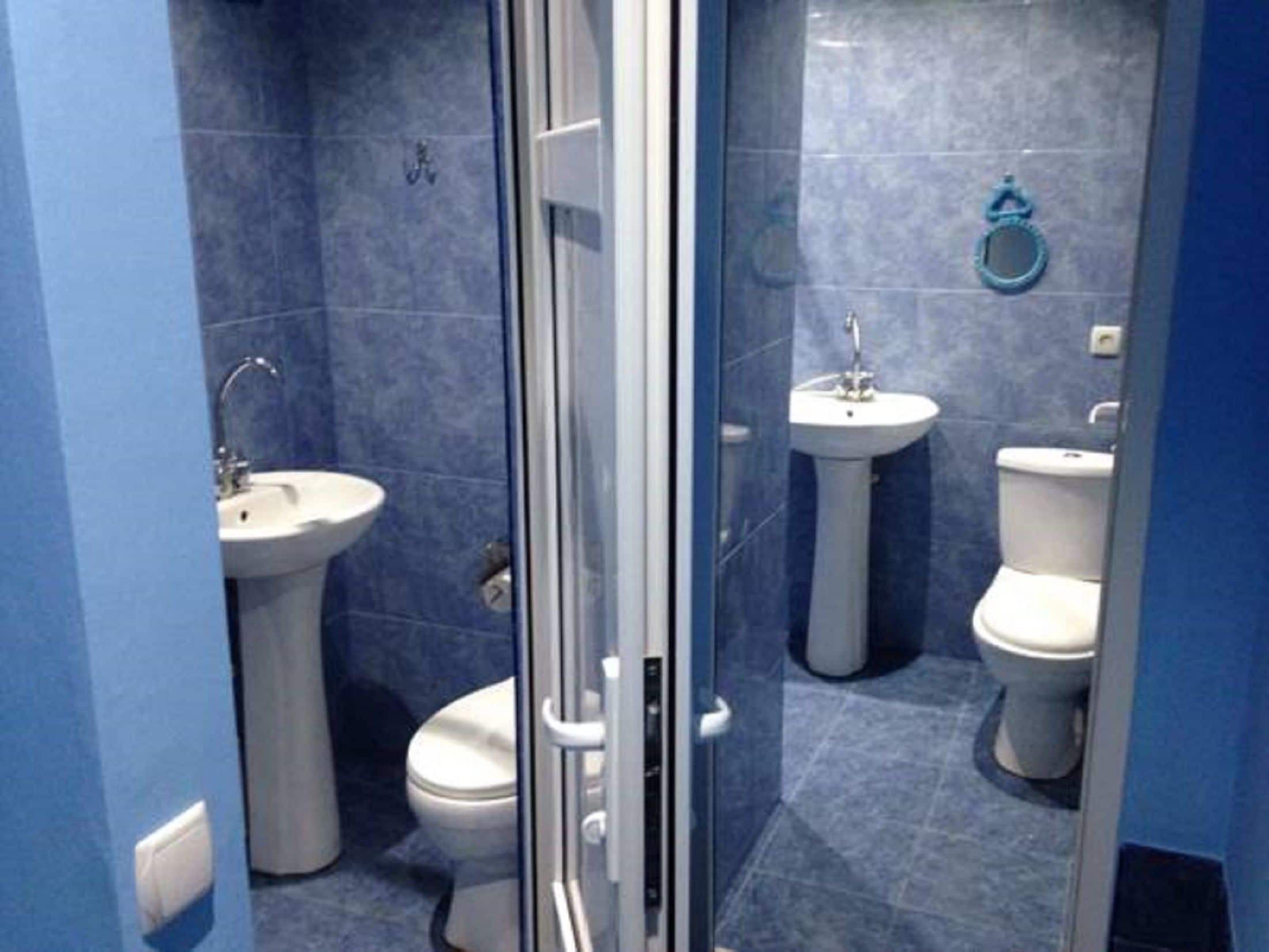 A bathroom with a glass shower enclosure, two sinks, and two toilets.