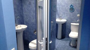 A bathroom with a glass shower enclosure, two sinks, and two toilets.