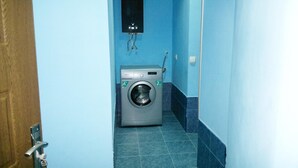 A laundry room with a front-loading washing machine, a wall-mounted heater, and a door with a modern handle. - Guest House Besarioni (Borjomi)