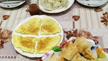 Una mesa servida con platos de comida, incluyendo lo que parecen albóndigas, un plato con cobertura verde y un plato con un guiso amarillo. También hay panes planos y un vaso pequeño de un líquido oscuro, posiblemente té.