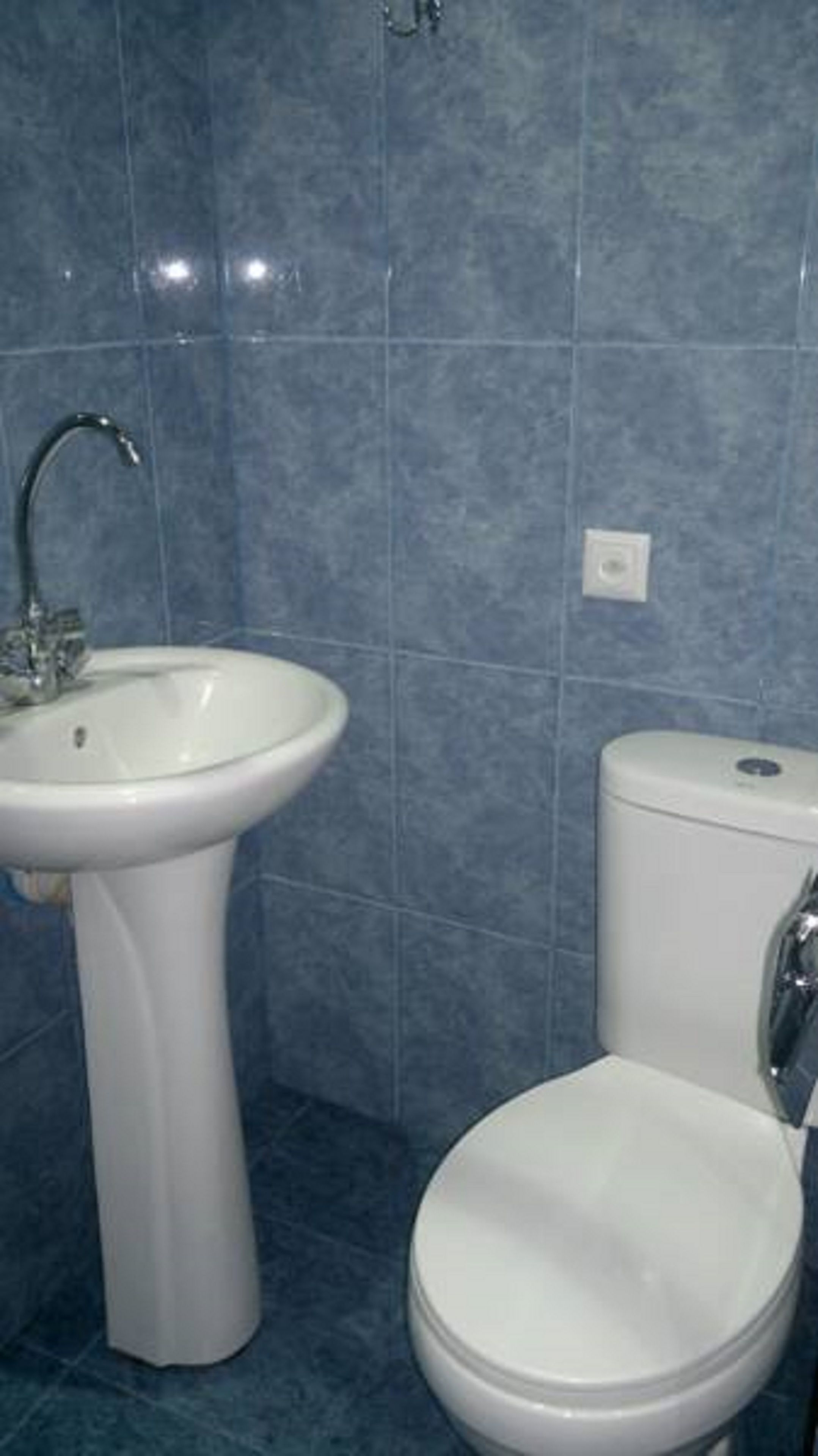 A bathroom with a white pedestal sink, a toilet, and blue-tiled walls.