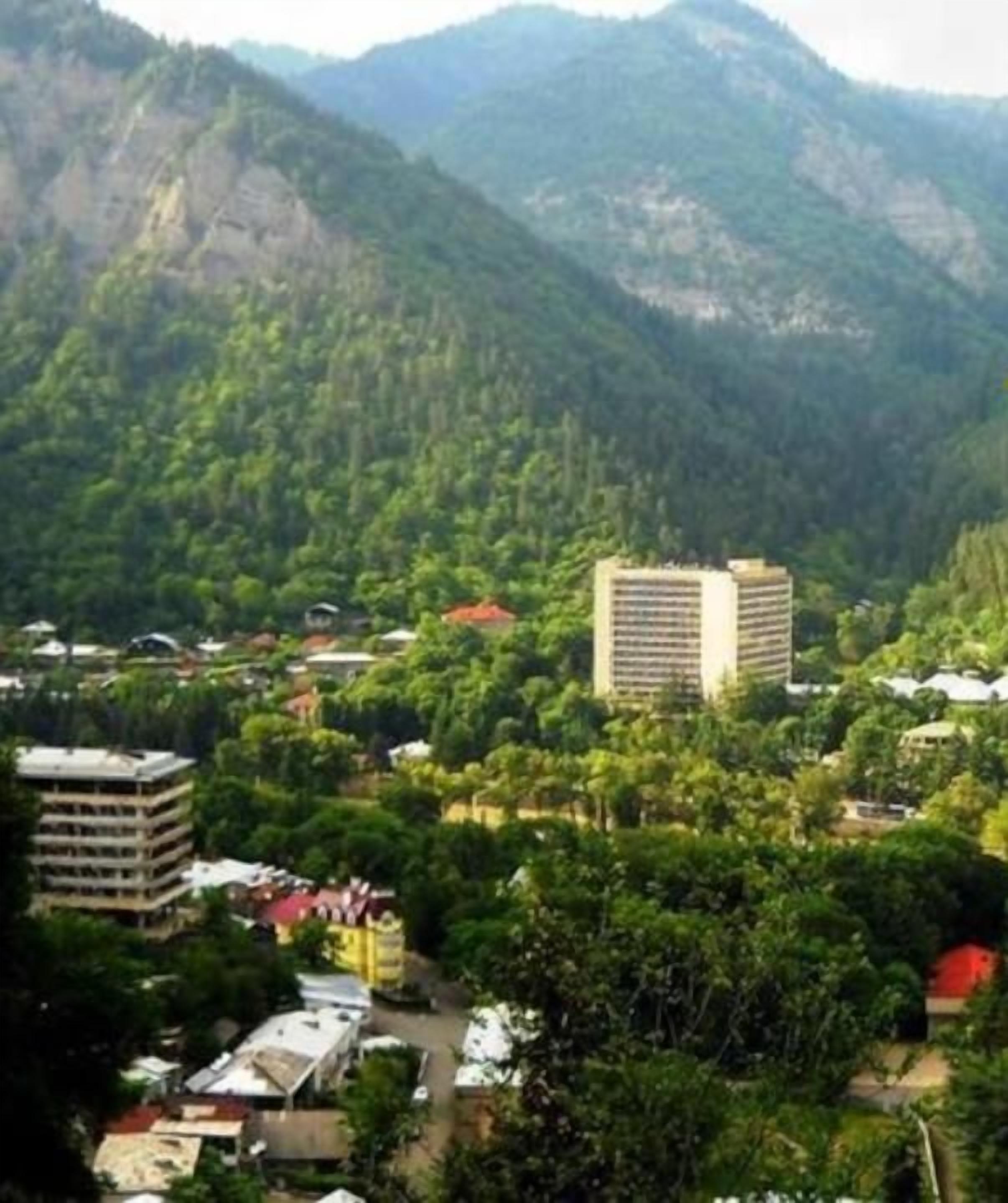 A mountainous landscape with a town nestled among the hills, featuring a prominent multi-story building and various smaller structures.
