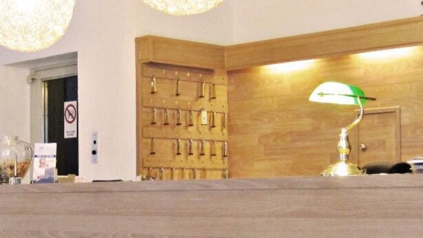 A reception desk with a wooden finish, a green desk lamp, and a wall-mounted display of keys. - Hotel Luise (Essen)