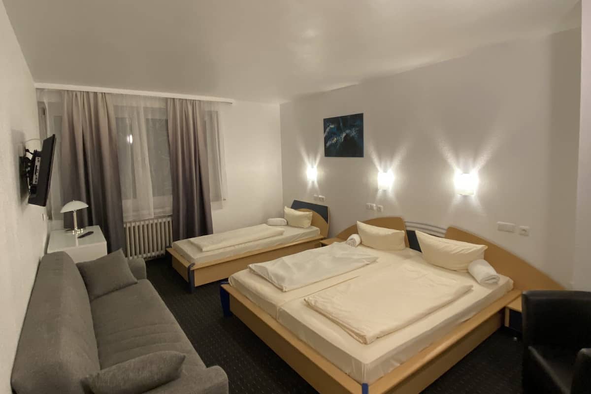 Habitación de hotel con dos camas individuales, un sofá, una silla, un escritorio y una ventana con cortinas.