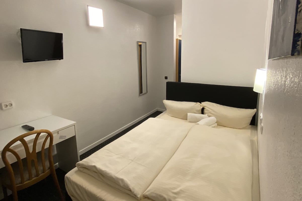 Habitación de hotel con cama, escritorio con silla, televisor de pantalla plana en la pared y espejo.