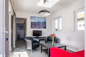 A modern living room with a cityscape painting, a flat-screen TV, a dining table, and a red sofa.