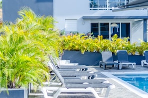 Un área junto a la piscina con sillas de descanso y plantas tropicales.