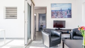 Ein modernes Wohnzimmer mit Stadtbildgemälde, einem Flachbildfernseher, Ledersofas und einer Glastür zum Balkon.
