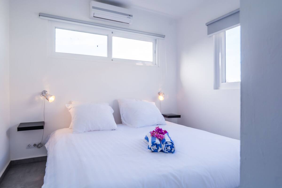 Une chambre d’hôtel avec un lit, deux lampes de chevet, une fenêtre et un appareil de climatisation.