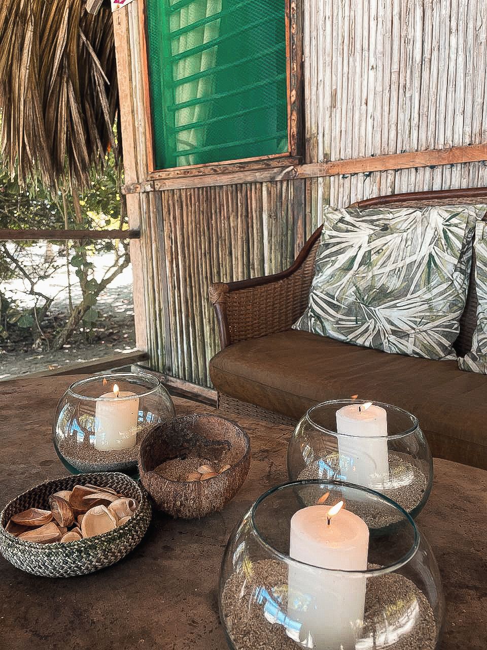 Un rincón acogedor con un sofá de mimbre, un ventanal verde y una almohada con motivos tropicales.