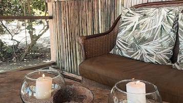Un rincón acogedor con un sofá de mimbre, un ventanal verde y una almohada con motivos tropicales.