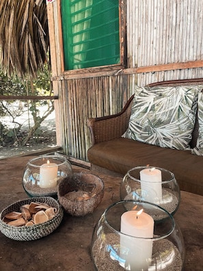 Un rincón acogedor con un sofá de mimbre, un ventanal verde y una almohada con motivos tropicales.