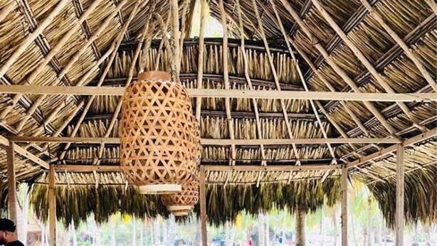Un bar junto a la playa con techo de paja, sillas de madera y una exhibición de frutas.