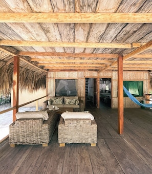 Un espacio de descanso techado al aire libre con mobiliario de mimbre, una hamaca y vista a un dormitorio.