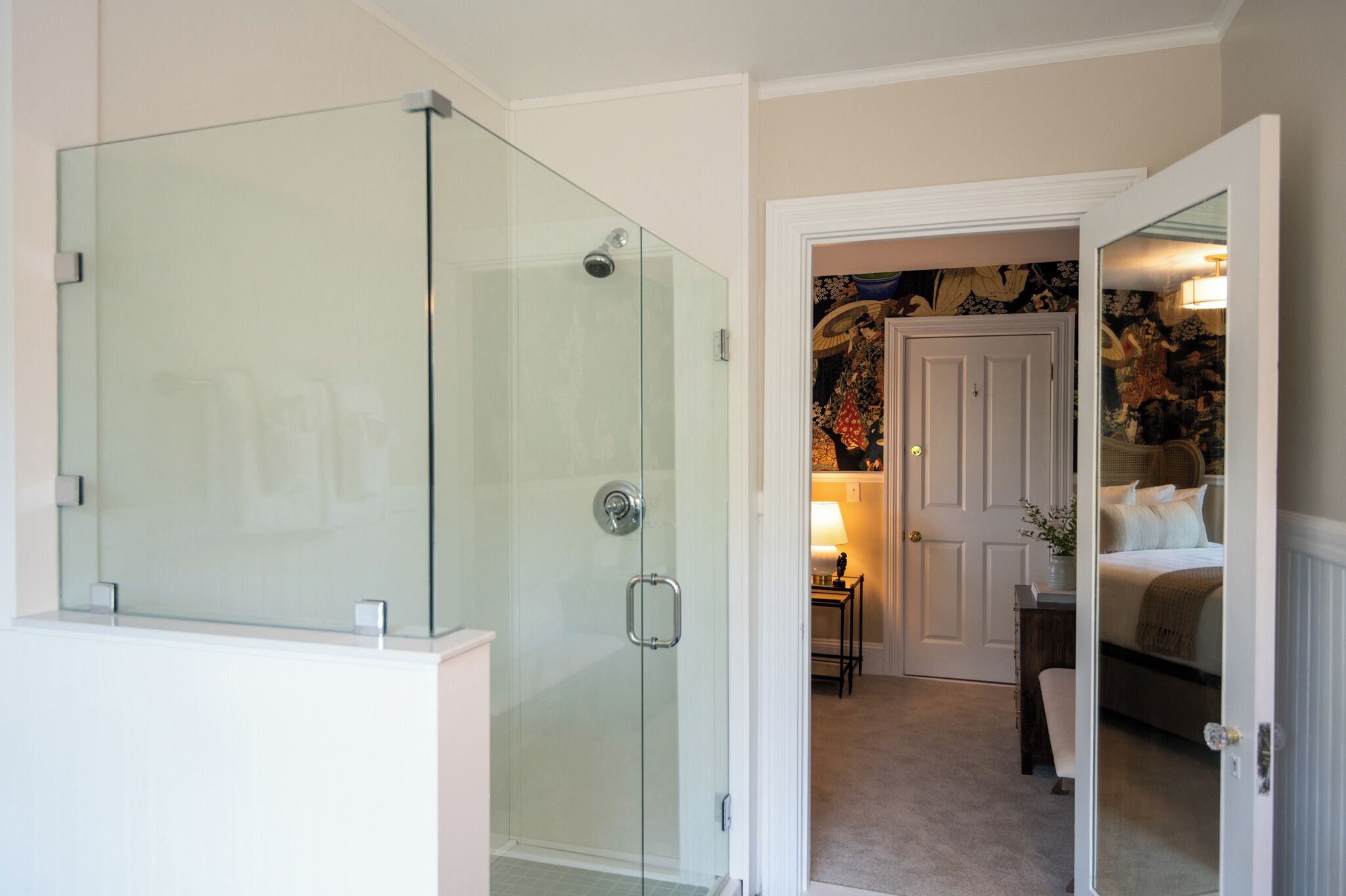 Ein modernes Badezimmer mit Duschkabine aus Glas und ein sichtbarer Schlafbereich mit Bett und Nachttisch.
