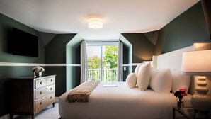Un dormitorio con una cama grande, un aparador, una mesita de noche con lámpara y vistas al exterior a través de una ventana.