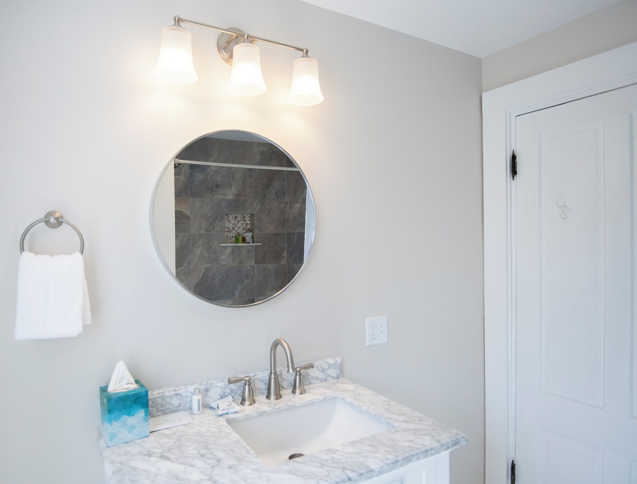 A bathroom with a round mirror, a sink with a marble countertop, and a towel rack.