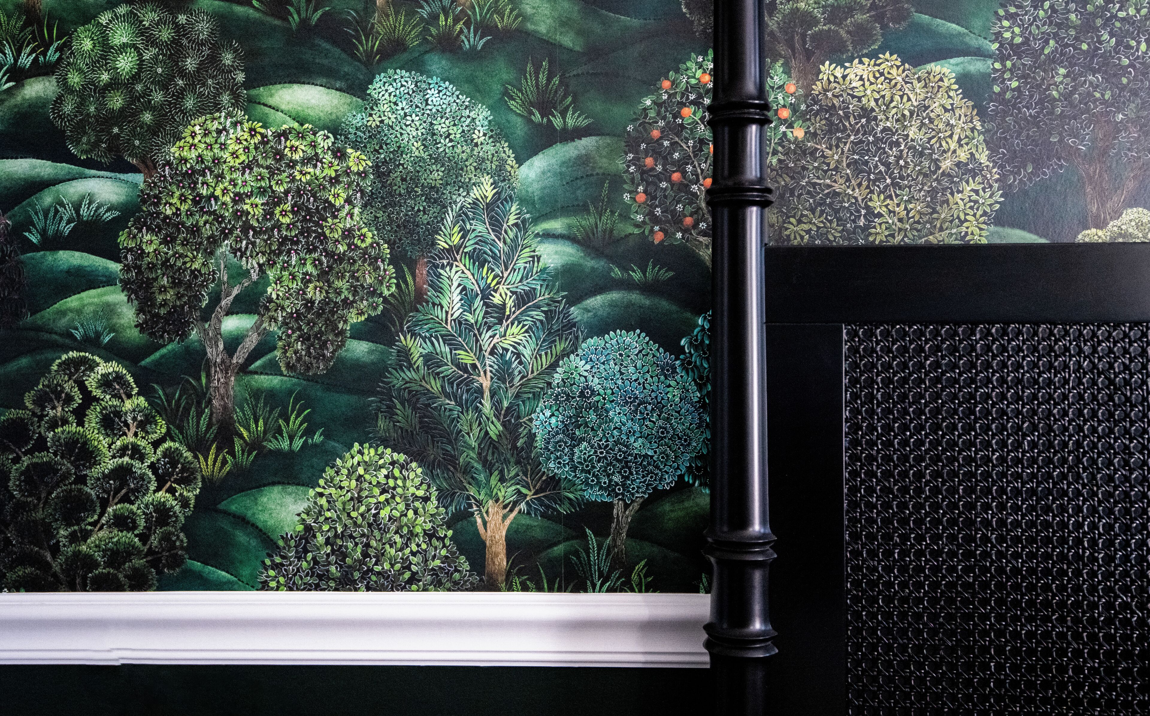 A window with a view of a lush garden, a black metal pole, and a textured wall.