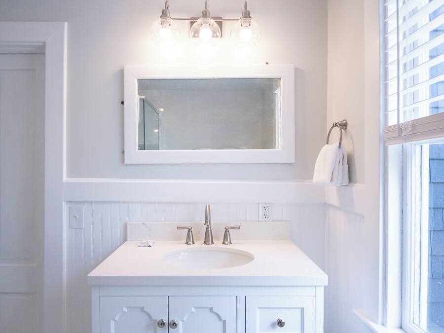 Une salle de bain avec un meuble-lavabo blanc, un grand miroir et une fenêtre avec des stores.