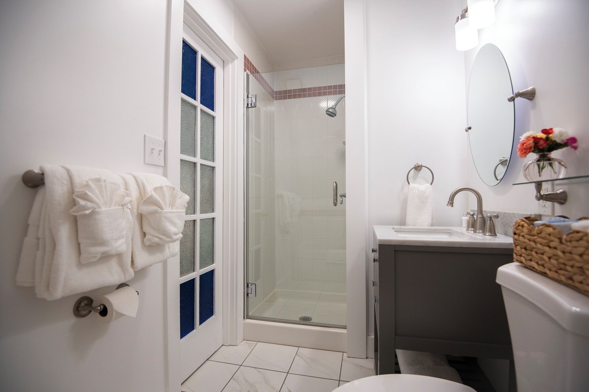 A bathroom with a glass shower enclosure, a sink with a mirror, and towels hanging on a rack.