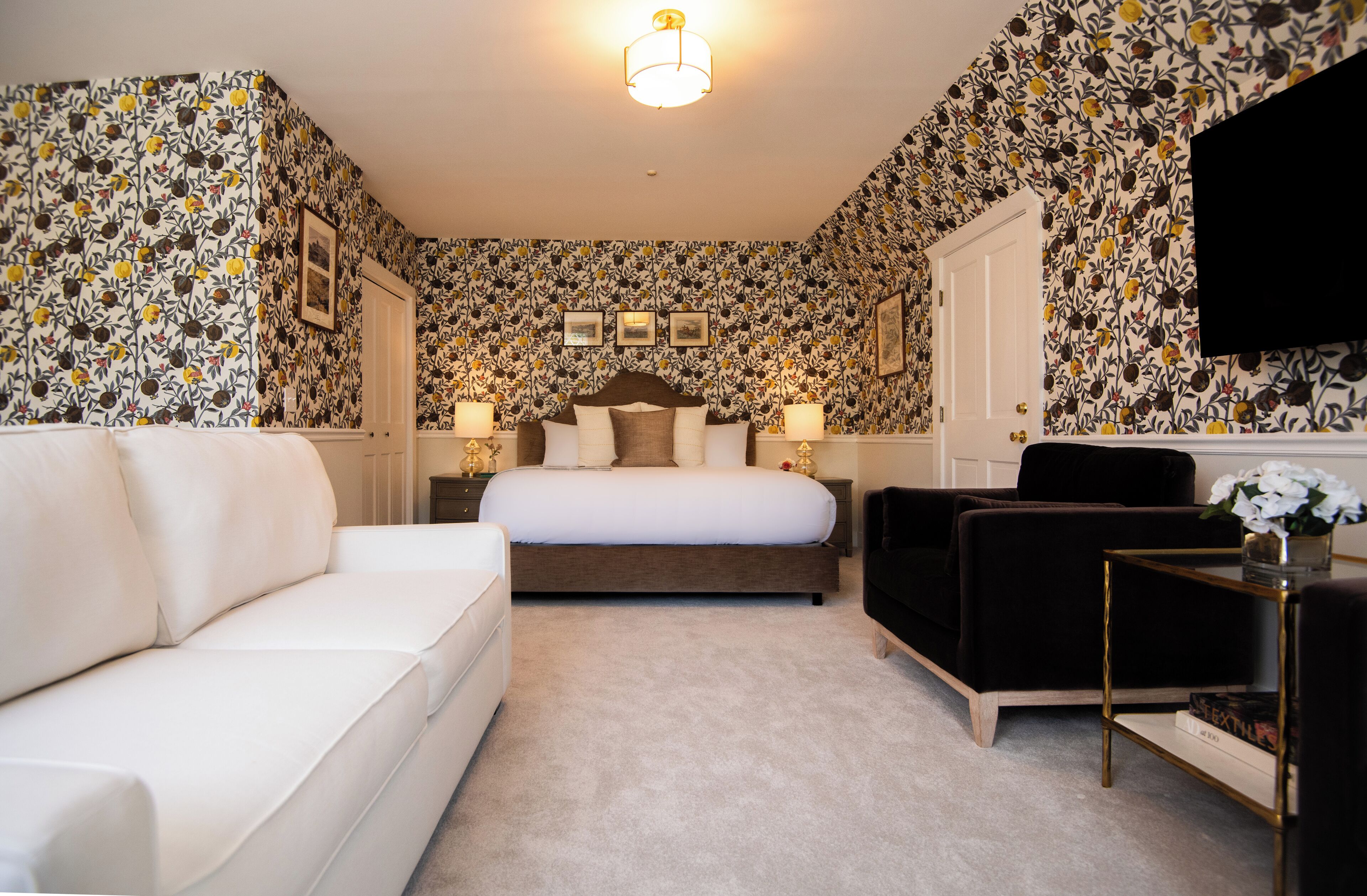 Een hotelkamer met een groot bed, een witte bank, een zwarte fauteuil en een kleine tafel met een bloevas.