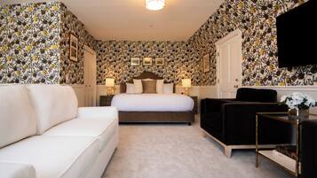 Een hotelkamer met een groot bed, een witte bank, een zwarte fauteuil en een kleine tafel met een bloevas.