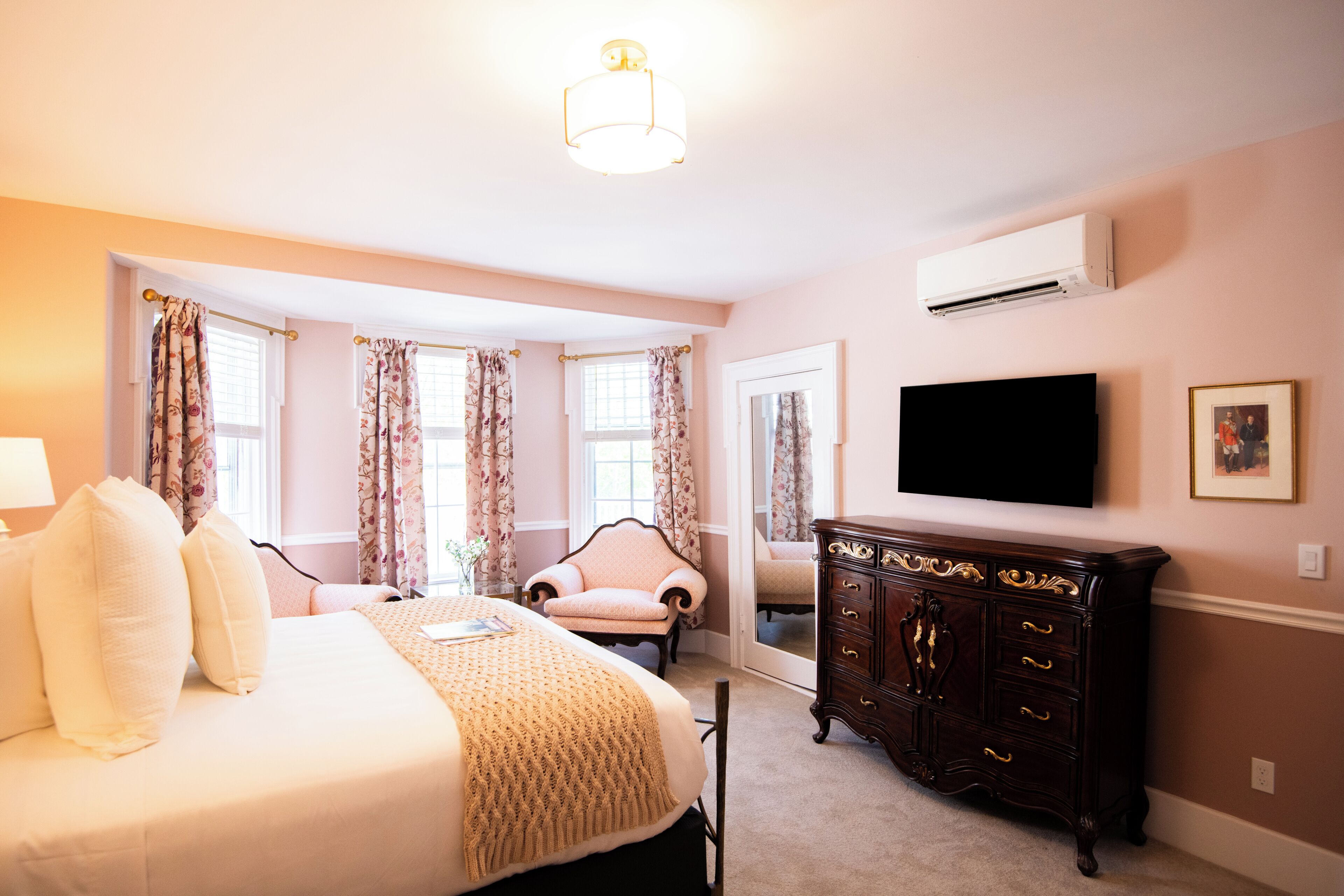 A bedroom with a bed, a dresser, a chair, a television, and an air conditioning unit.