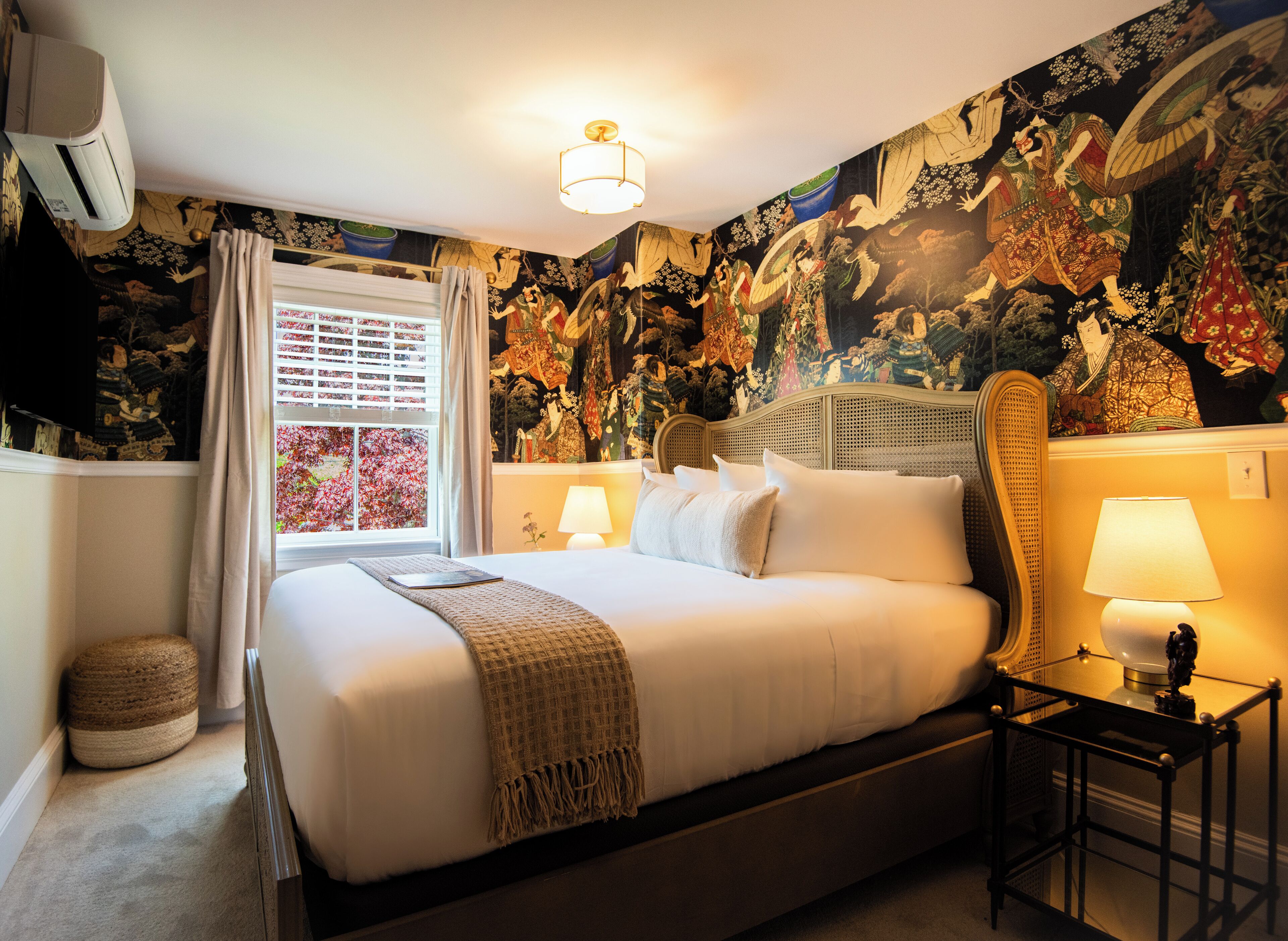 A hotel room with a large bed, two bedside lamps, a window with curtains, and a wall with a detailed tapestry.